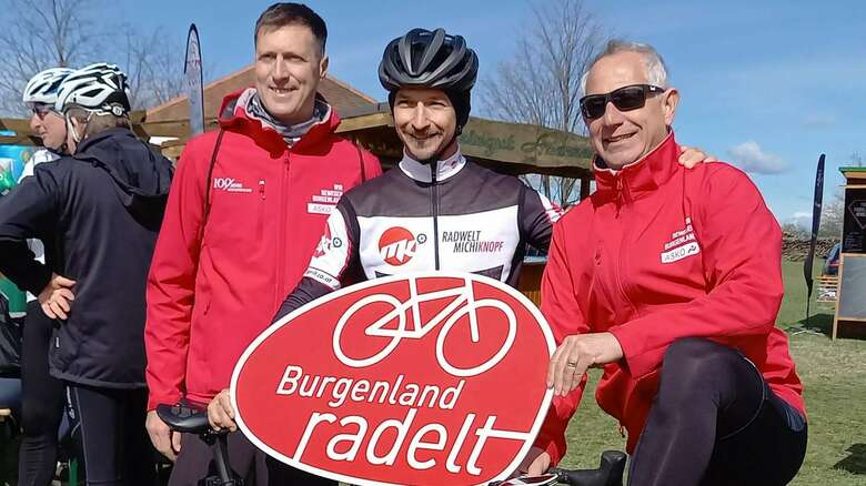 Drei Radfahrer halten ein Schild mit der Aufschrift Burgenland Radelt
