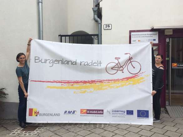 Leiterin der Mobilitätszentrale Burgenland Christine Zopf-Renner  zeigt mit der Mitarbeiterin Lisa Liszt den neuen Projektbanner