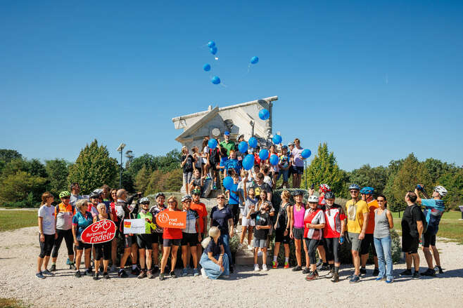 Radgruppe vor Mahnmal; Luftballons steigen