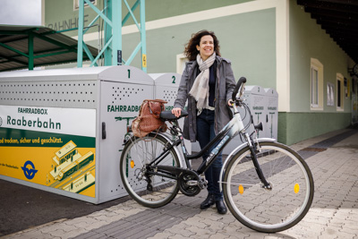 Frau mit Fahrrad vor Radboxen auf Bahnhof